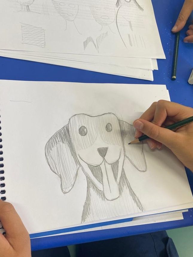Aluno desenhando a lápis em prancheta na aula de desenho