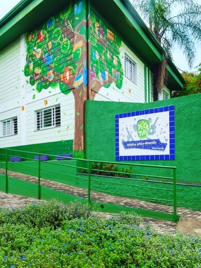 Fachada da TaCaTum, com a árvore pintada na parede e o muro verde